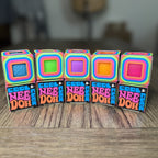 A row of five NeeDoh Cool Cube boxes showing blue, green, purple, orange and pink cubes