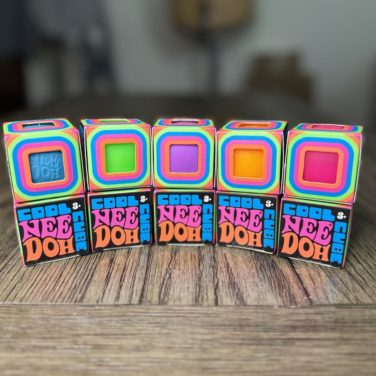 A row of five NeeDoh Cool Cube boxes showing blue, green, purple, orange and pink cubes